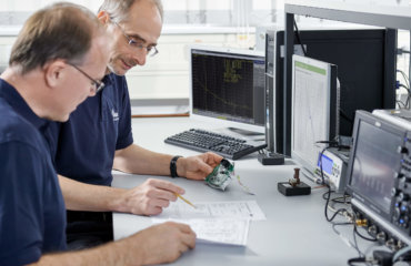 Two men analyze an electronic circuit