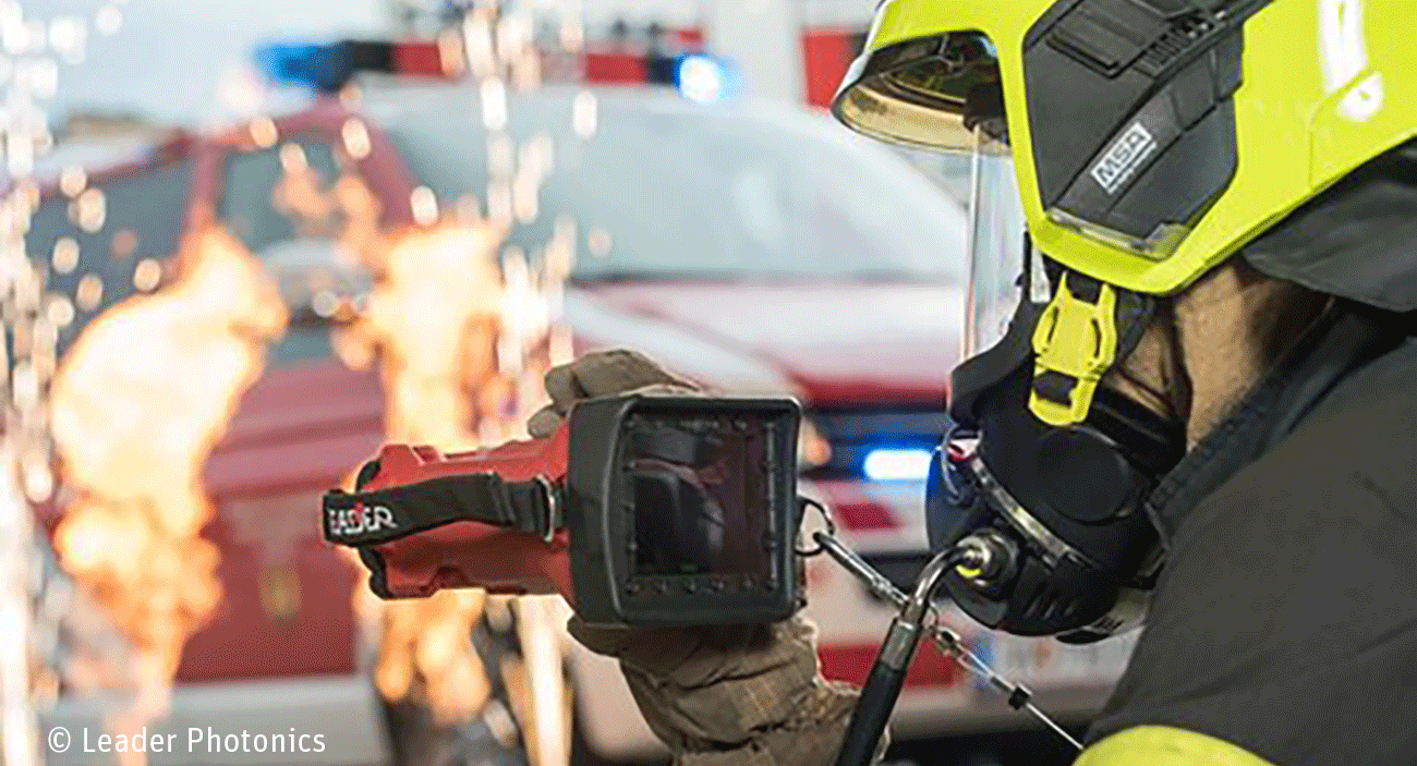 Leader_Teaser Ein Feuerwerhmann benutzt eine Wärmebildkamera. Im Hintergrund ist ein Feuerwehrauto zu sehen und es sprühen Funken